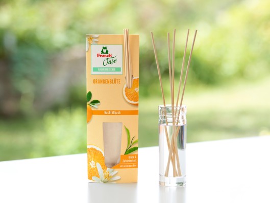 A room fragrance glass bottle with reed diffusers stands nex