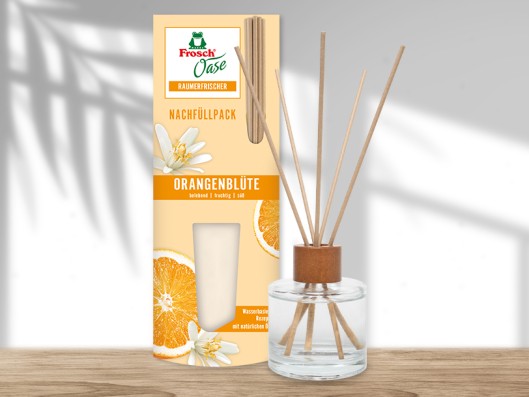 A Frosch Oase glass bottle stands on a table and is filled with water and flowers