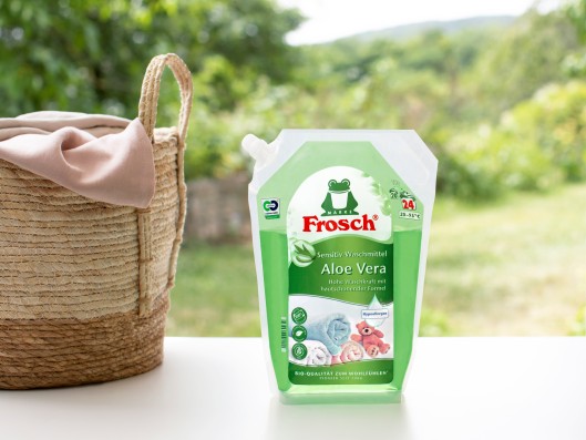 A Frosch sensitive detergent aloe vera pouch stands next to a basket of laundry