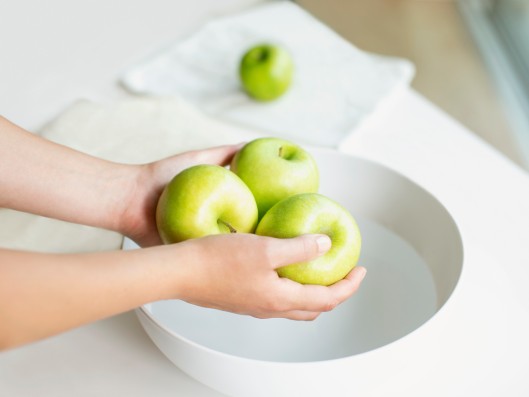 Zwei Hände halten drei Äpfel über einer Schüssel mit Wasser